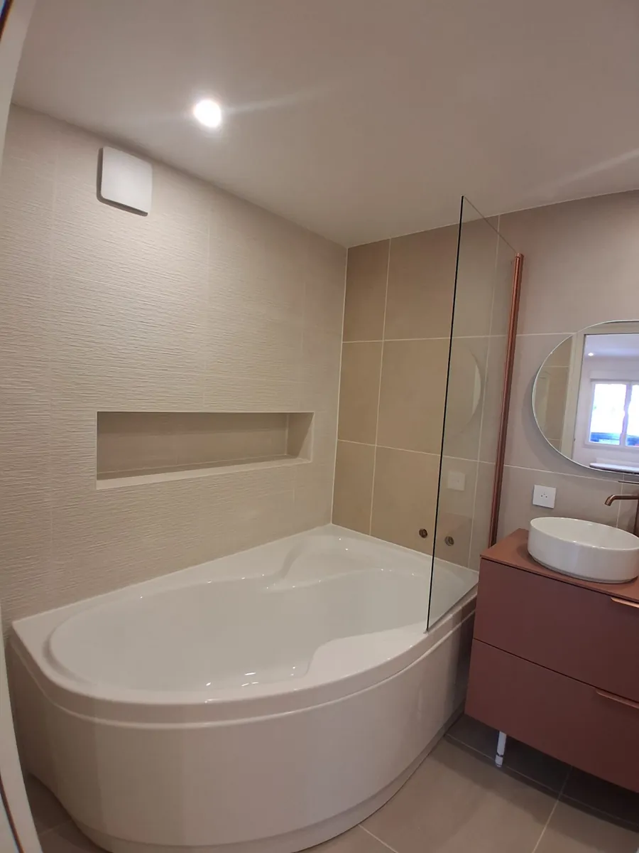 Baignoire d'angle avec niche murale carrelée et pare-bain vitré, salle de bain en Essonne