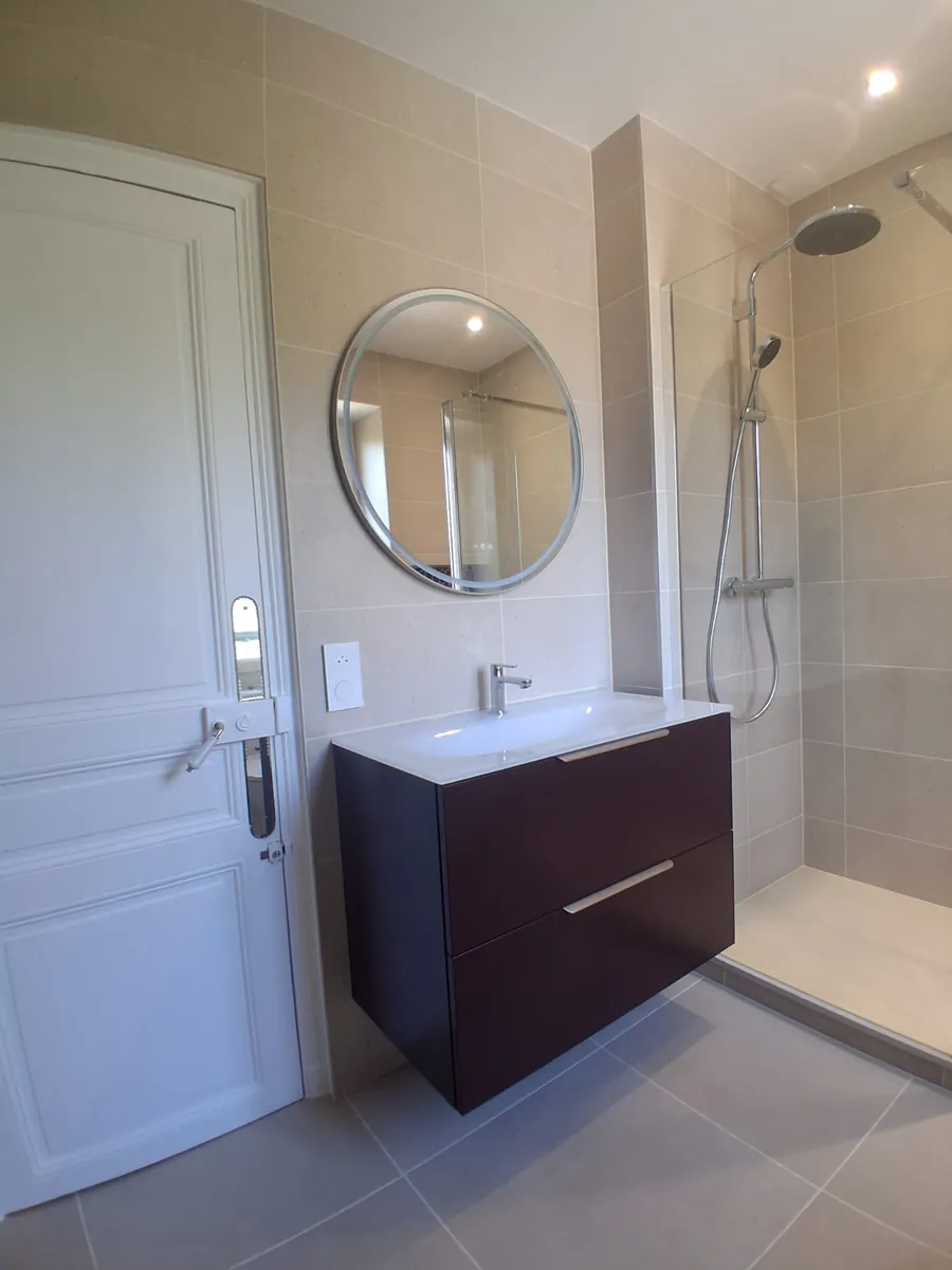 Meuble vasque suspendu et miroir rond dans une salle de bain rénovée en Essonne